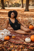Woman in a black swimsuit sitting on a blanket with pumpkins and a book in an autumn setting