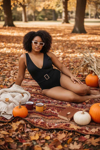 Woman in a black swimsuit sitting on a blanket with pumpkins and a book in an autumn setting