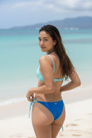 Woman in a ocean blue bikini standing on a beach with clear water and sky in the background